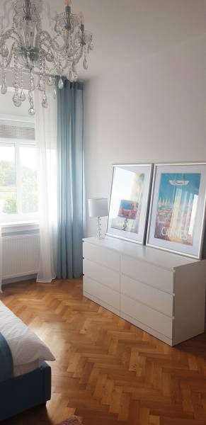 A bedroom in a studio apartment with a cabinet, chandelier, and wooden decor flooring.