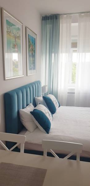 Bedroom in a studio apartment with a bed, turquoise headboard, paintings, and light curtains.