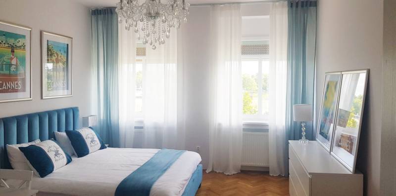 Bright bedroom in a one-room apartment with wood-patterned flooring and turquoise curtains.