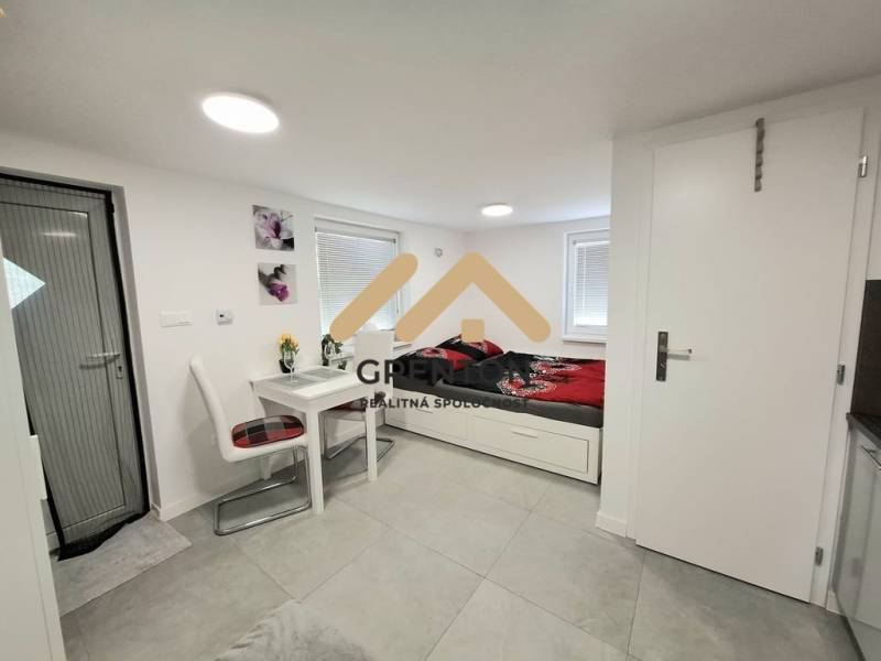 Interior of a cottage with a dining table, chairs, and a bed on a light floor.