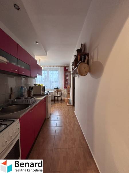 A kitchen in a two-room apartment with a wooden decor floor, with a dining area in the background.