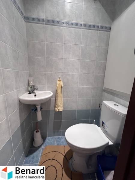 A bathroom in a 2-room apartment with a toilet and a sink, surrounded by light tiles.