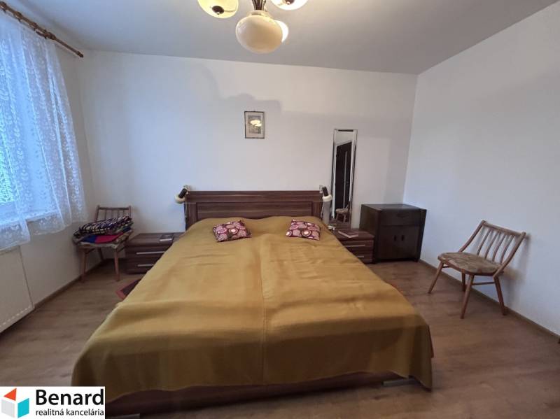 Bedroom in a 2-room apartment with a bed, chairs, and a wooden decor floor.