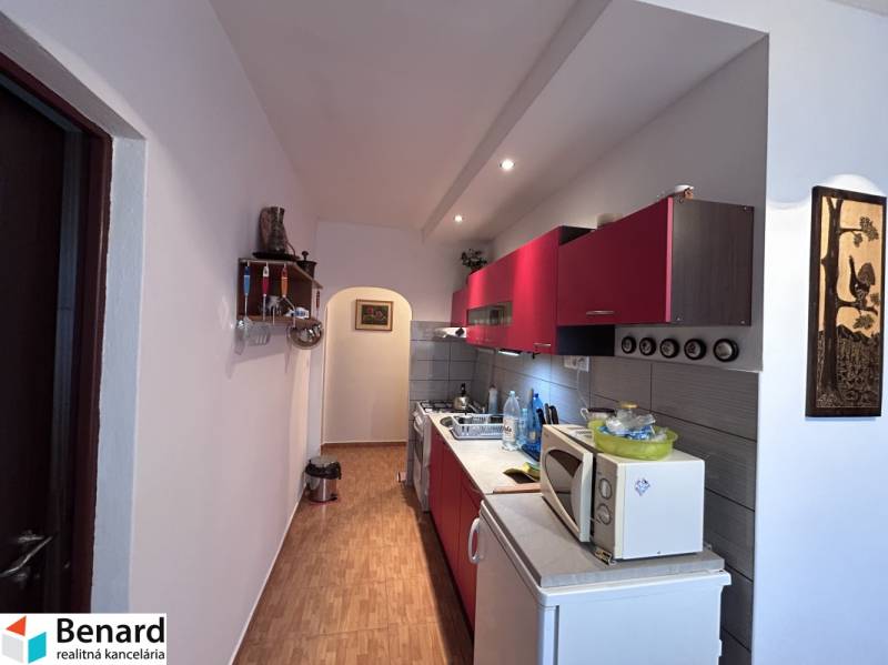 A kitchen with red cabinets and a wood-patterned floor in a two-room apartment.