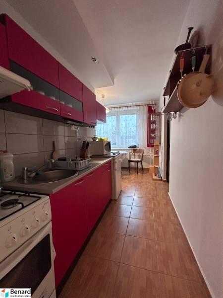 A kitchen in a 2-room apartment with red cabinets and a wood-patterned floor.