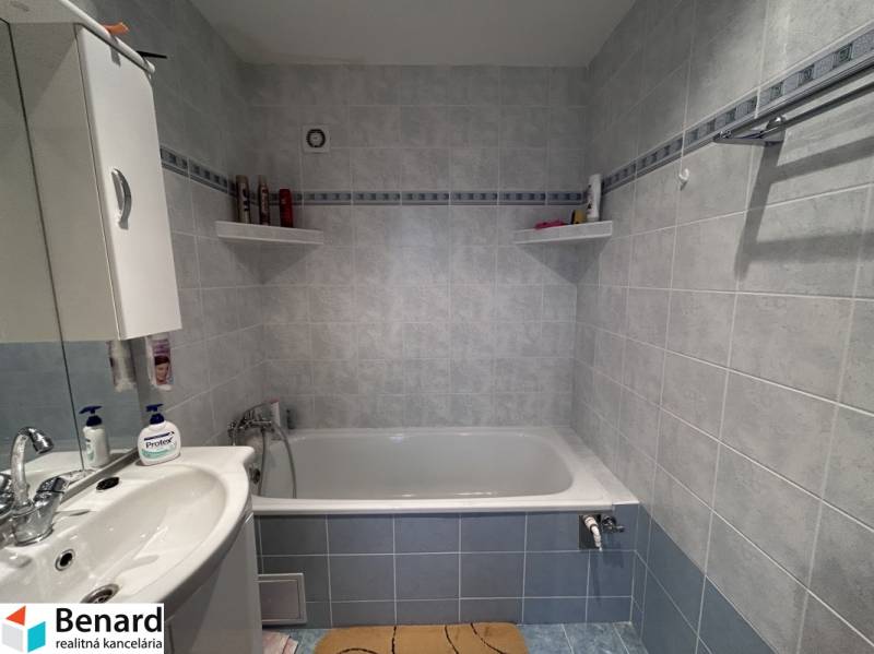 A bathroom with a bathtub, sink, and shelves in a 2-room apartment with blue tiles.