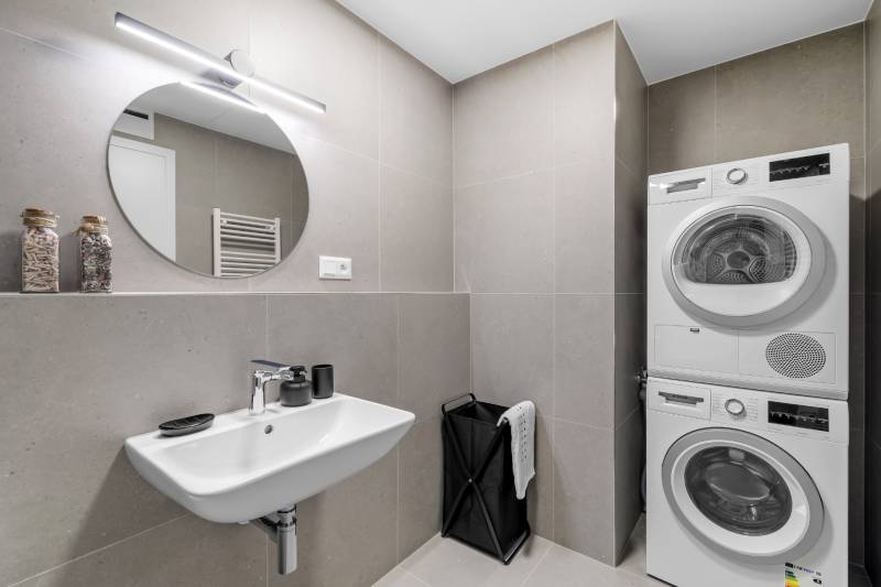 Bathroom in a 2-room apartment with a sink, washing machine, and dryer. Concrete tiles.