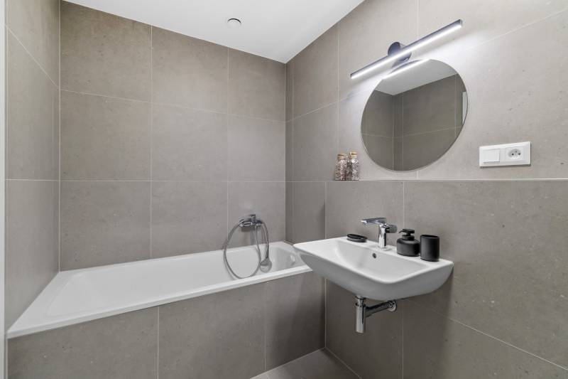 Bathroom in a 2-room apartment with a shower, sink, and round mirror.
