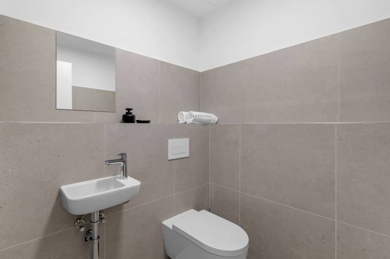 Bathroom in a 2-room apartment with a sink, toilet, and beige tiles.