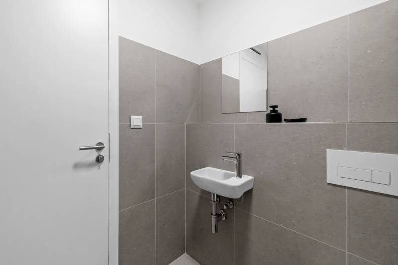 Bathroom in a 2-room apartment with a small sink, white tiles, and a mirror.