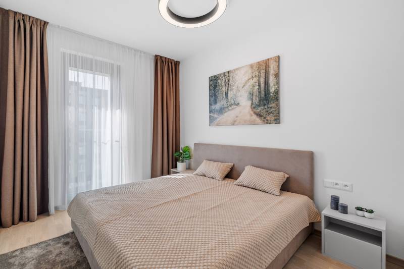 A bedroom with a large bed, curtains, and a wooden decor floor in a 2-room apartment.