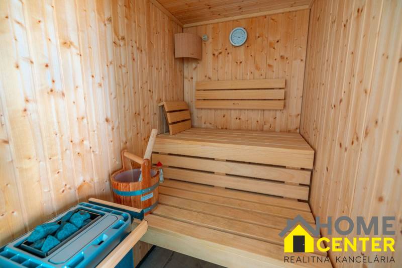Wooden sauna in the villa with benches, a thermometer, and a water bucket.