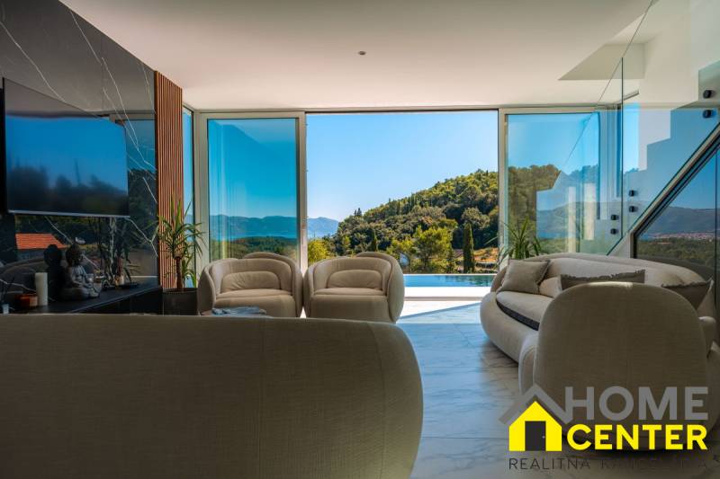 Interior of a villa with large windows, view of greenery and pool.