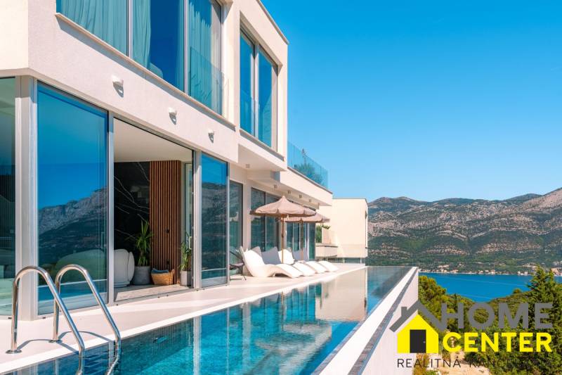 A villa in Korčula with glass walls, a pool, and a view of the mountains.