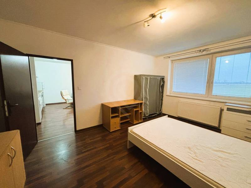 A bedroom in a two-room apartment with a wooden decor floor and simple furniture.