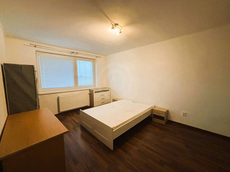 Bedroom in a two-room apartment with wood-patterned flooring, a bed, and a wardrobe.