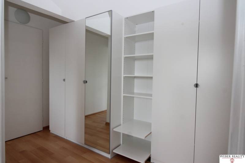 White built-in wardrobe with mirror and shelves in a studio apartment.