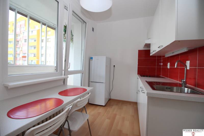 A kitchen in a studio apartment with red tiles, a wood-patterned floor, and a refrigerator.