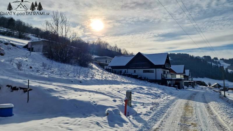 A snowy street in Mýto pod Ďumbierom with a view of houses and the surrounding landscape.