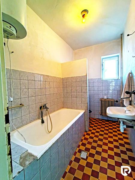 A bathroom in a family house with a bathtub, a sink, a radiator, and checkered tile flooring.