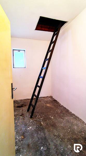 Attic in a family house with a ladder leading to a ceiling opening.