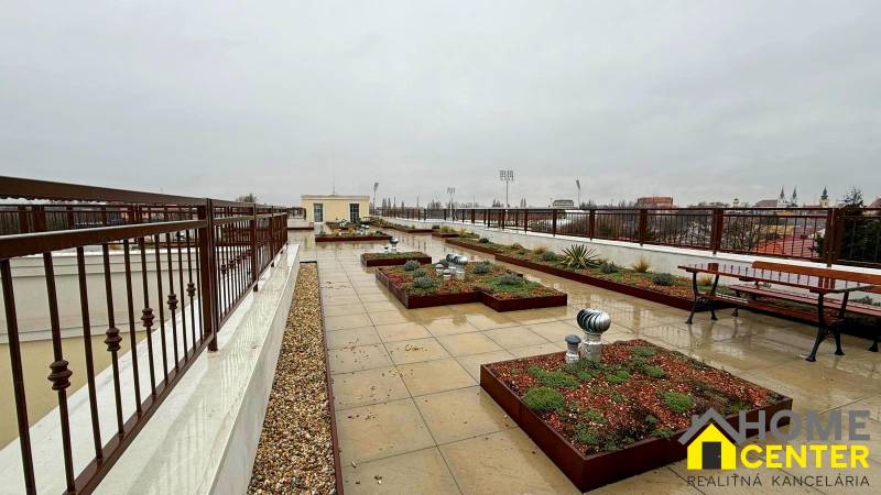 A terrace with a view of Komárno, at a 2-room apartment, with plants and benches.