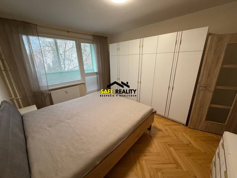 Bedroom in a three-room apartment with a wooden decor floor and a large built-in wardrobe.