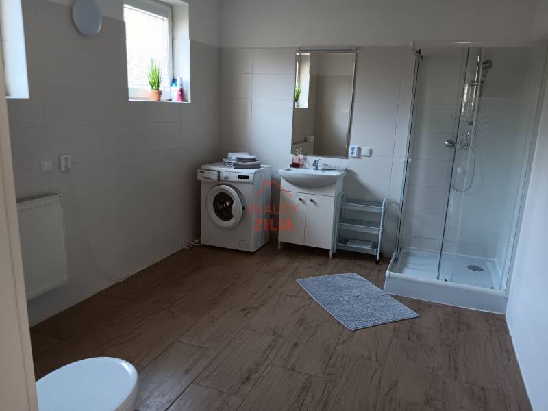 Bathroom with a washing machine, shower corner, and sink in a family house with a wooden decor floor.