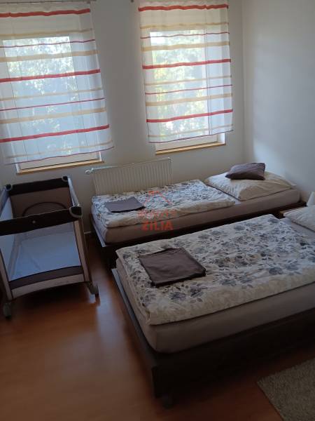 A crib and two beds in a bedroom with wood-patterned flooring.