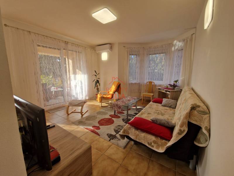 Living room of a family house with a television, sofa, coffee table, and large windows with curtains.