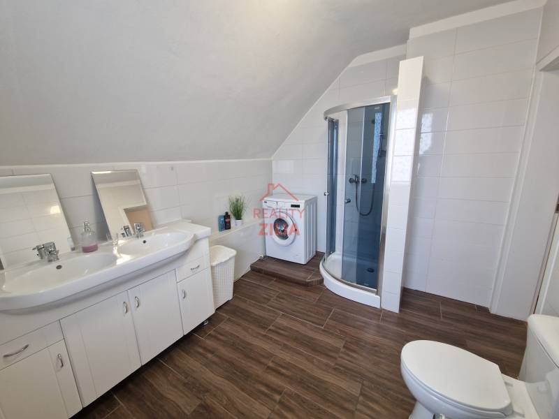 A bathroom in a family house with a sink, a shower corner, and a floor with a wooden decor.