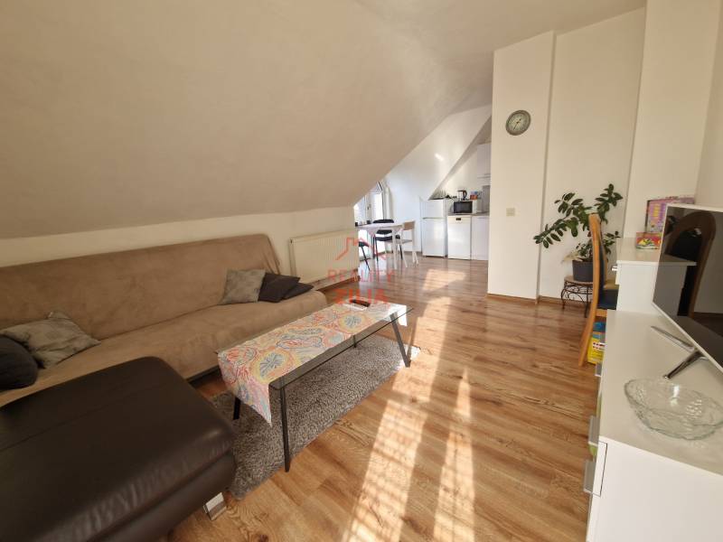 Attic living room in a family house with a sofa, dining table, and wooden decor flooring.