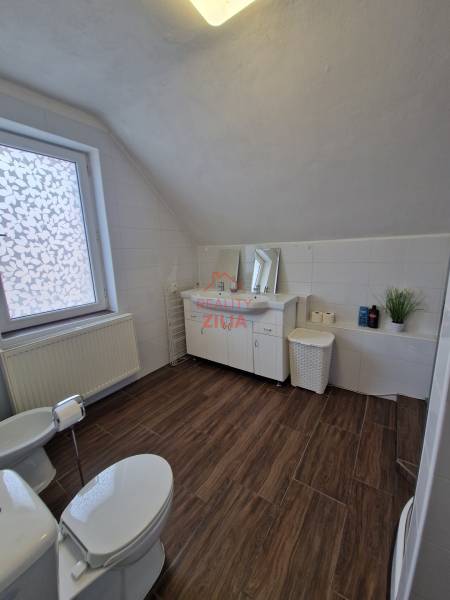 A bathroom with a wood-patterned floor in a family house, equipped with a toilet, sink, and bathtub.