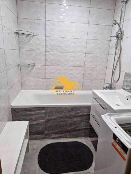 A bathroom in a 3-room apartment with a bathtub, shower, and washing machine on white tiles.