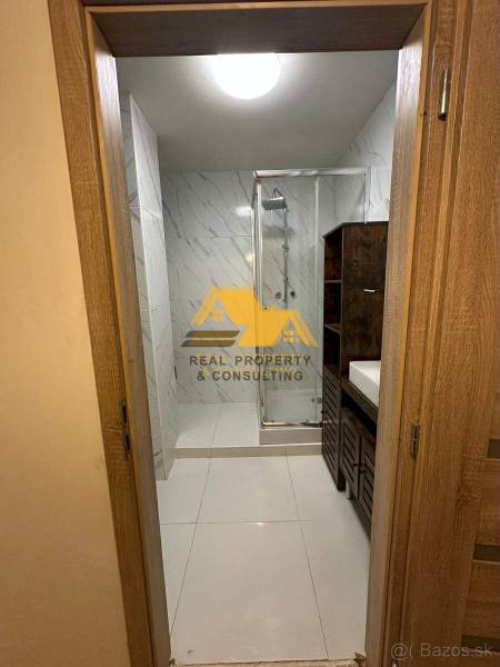 Bathroom with a shower and a sink in a 2-room apartment, with tiles in light tones.