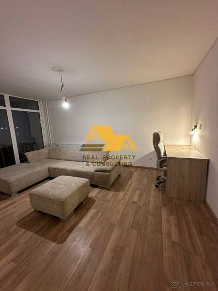 Living room of a two-room apartment with a wood-patterned floor, a corner sofa, and a table.