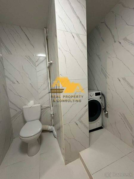 Bathroom in a 2-room apartment with a washing machine and toilet, tiled with a white tile design.