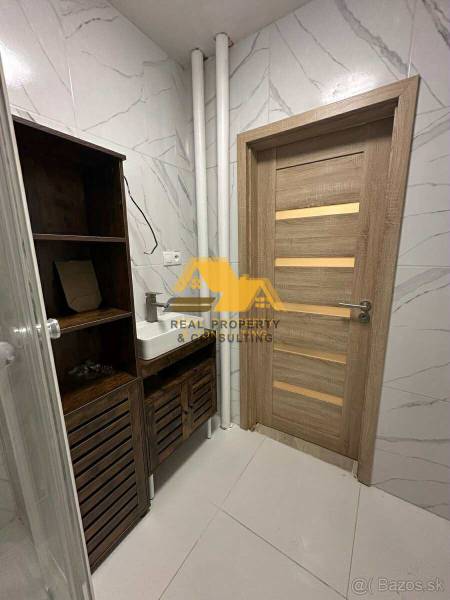 Bathroom in a 2-room apartment with a sink, cabinet, wooden door, and white tiles.