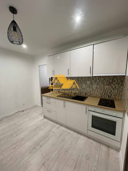 A kitchen in a studio apartment with a light-colored kitchen unit and a floor with a wood decor.