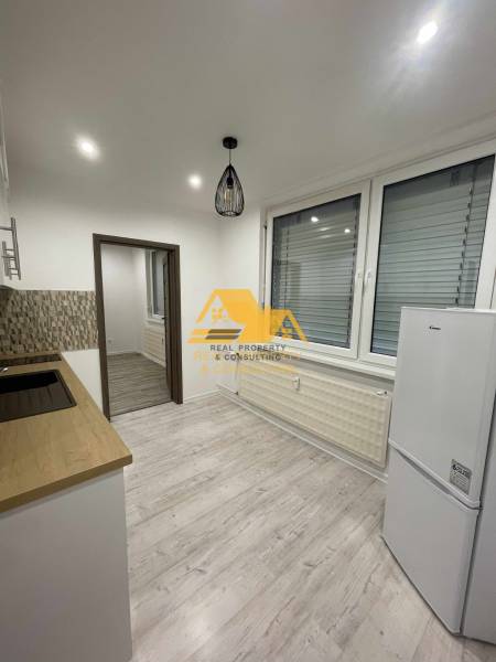 A kitchen in a studio apartment with a wood-patterned floor and white appliances.