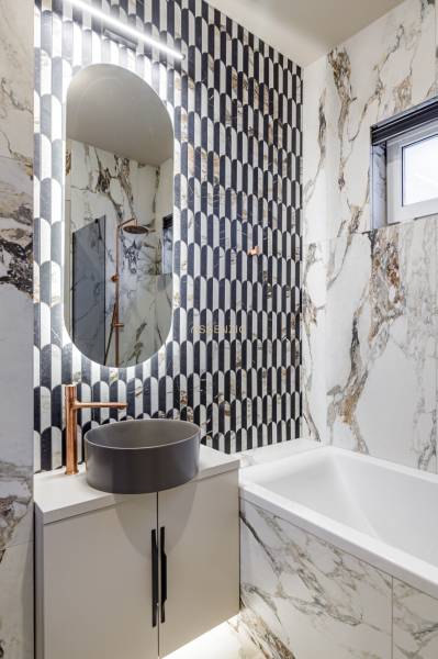 A bathroom with marble tiles, an oval mirror, and a freestanding sink in a 2-room apartment.