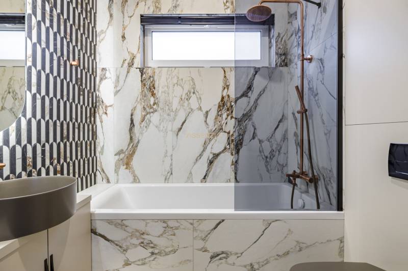 A bathroom in a 2-room apartment with designer tiles and a bathtub in a marble decor.