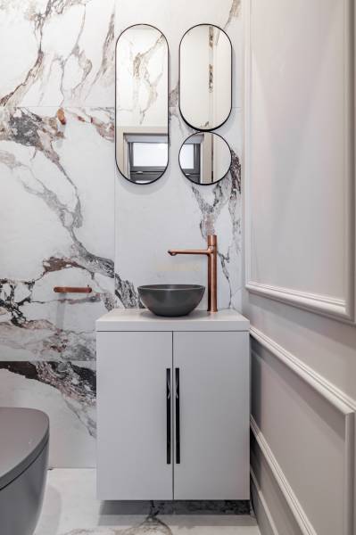Marble sink with round mirrors and a copper faucet in a 2-room apartment.