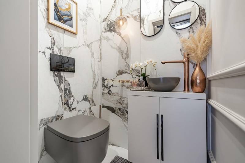 Bathroom in a 2-room apartment with marble walls, a stylish sink, and decorations.