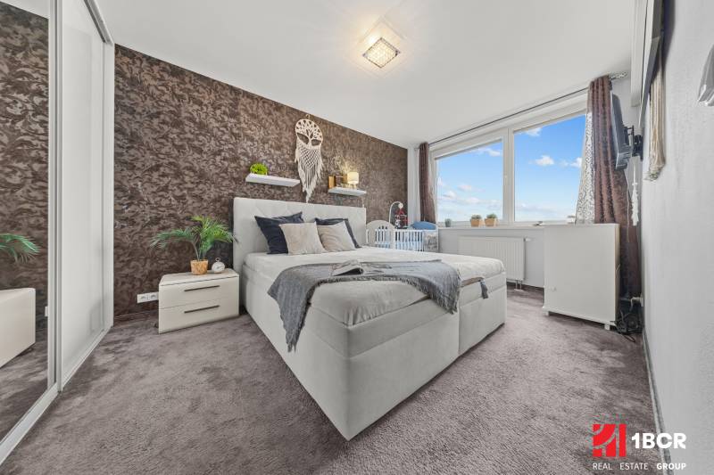 Bedroom in a 2-room apartment with a double bed, carpeted floor, and decorative wall.