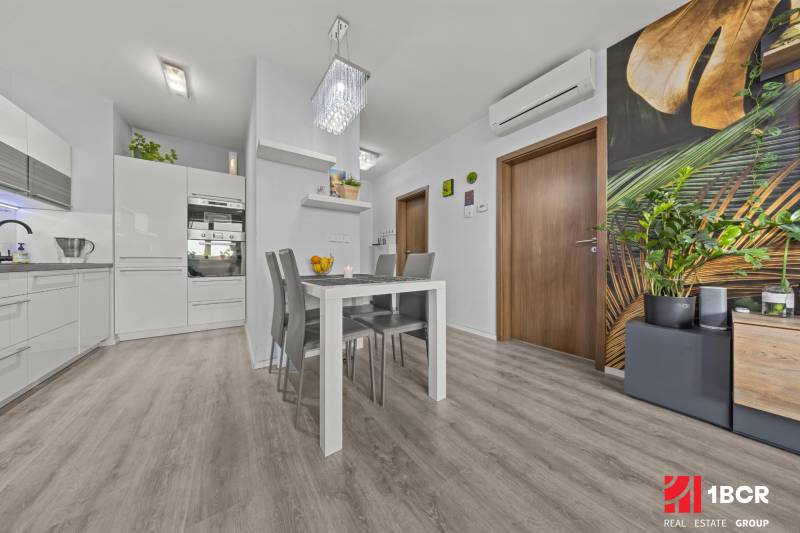 Dining area with a white table and gray chairs in a 2-room apartment, floor with wood decor.