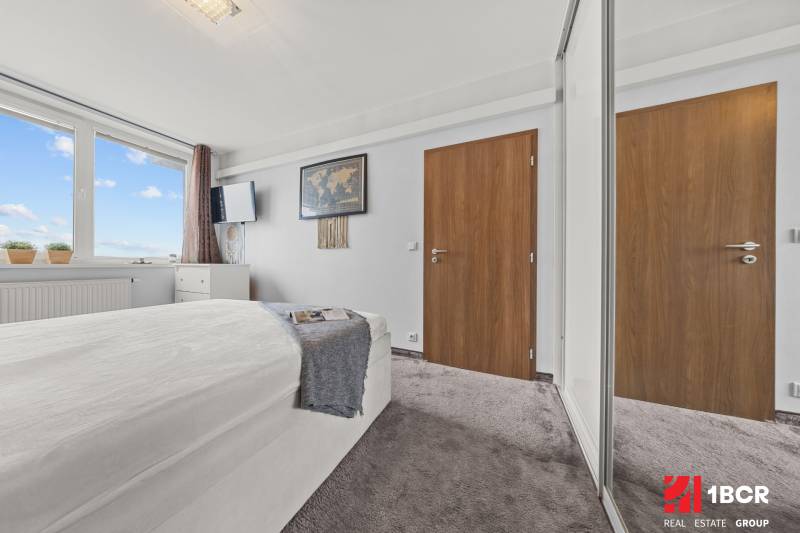 A bright bedroom with a bed, a large window, and a wardrobe in a 2-room apartment.