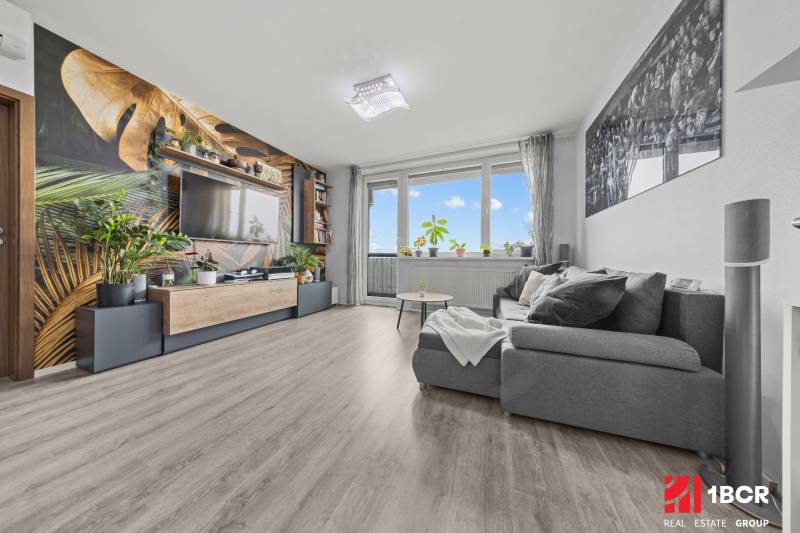 Living room with a comfortable sofa, wallpaper with a plant motif, and a wooden decor floor.