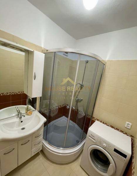 A bathroom in a one-room apartment with a bathtub, washing machine, and sink.