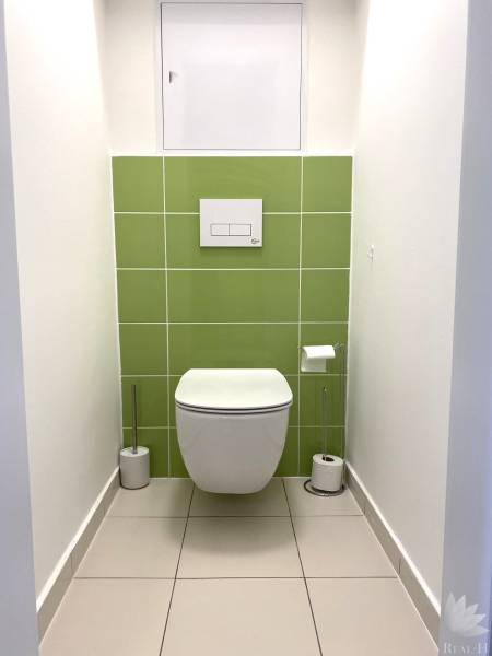 A toilet with white and green tiles in a three-room apartment.